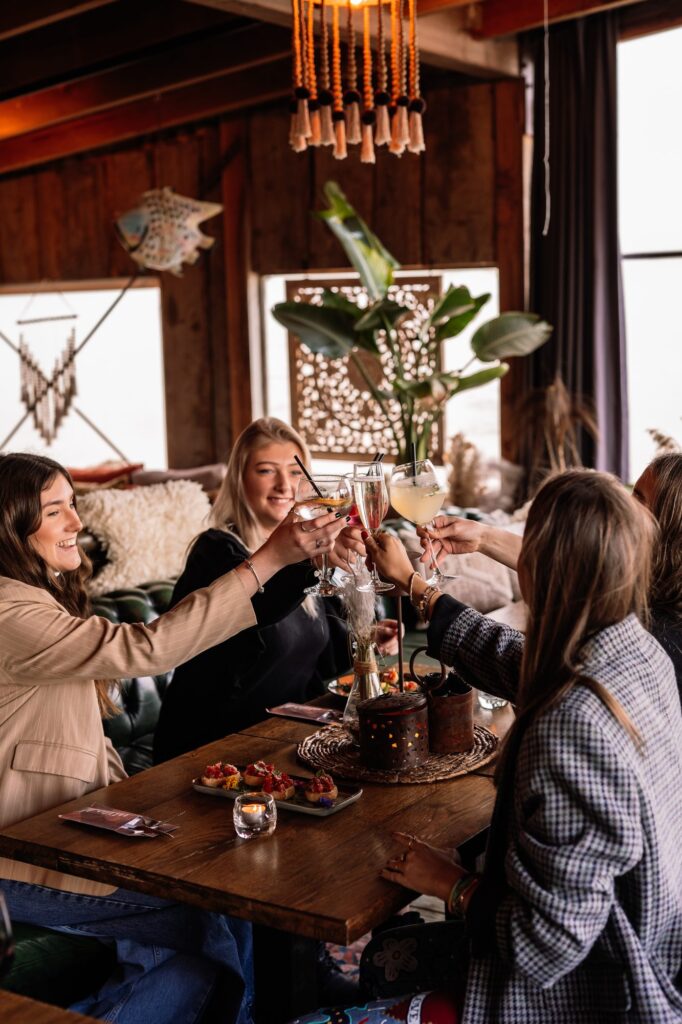 Vriendinnen proosten aan tafel in de lodge van strandtent R Port in Hoek van Holland